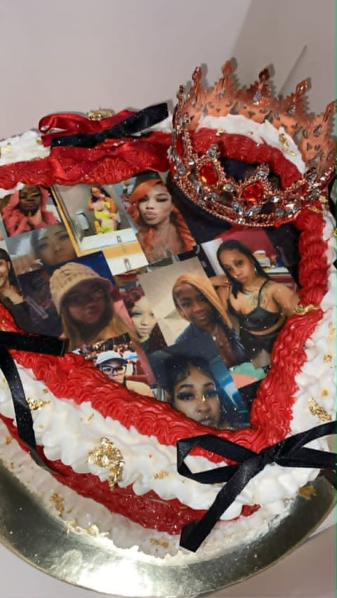 Decorative heart-shaped cake with red piped frosting, photo collage center, red crown decoration, and black ribbons on silver base