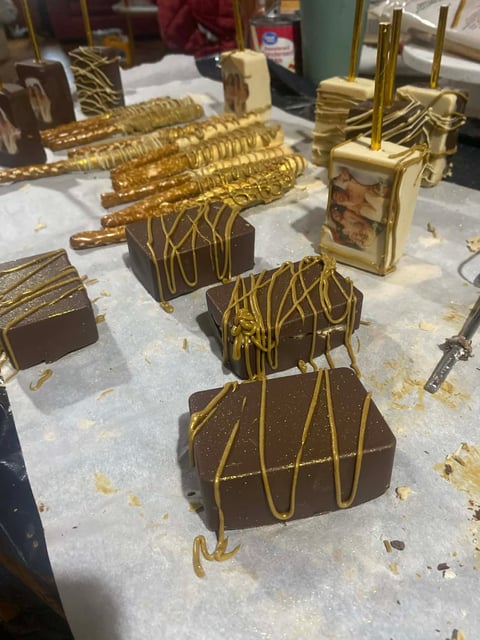 Artisanal chocolate confections drizzled with gold stripes on white parchment paper in a candy making workspace