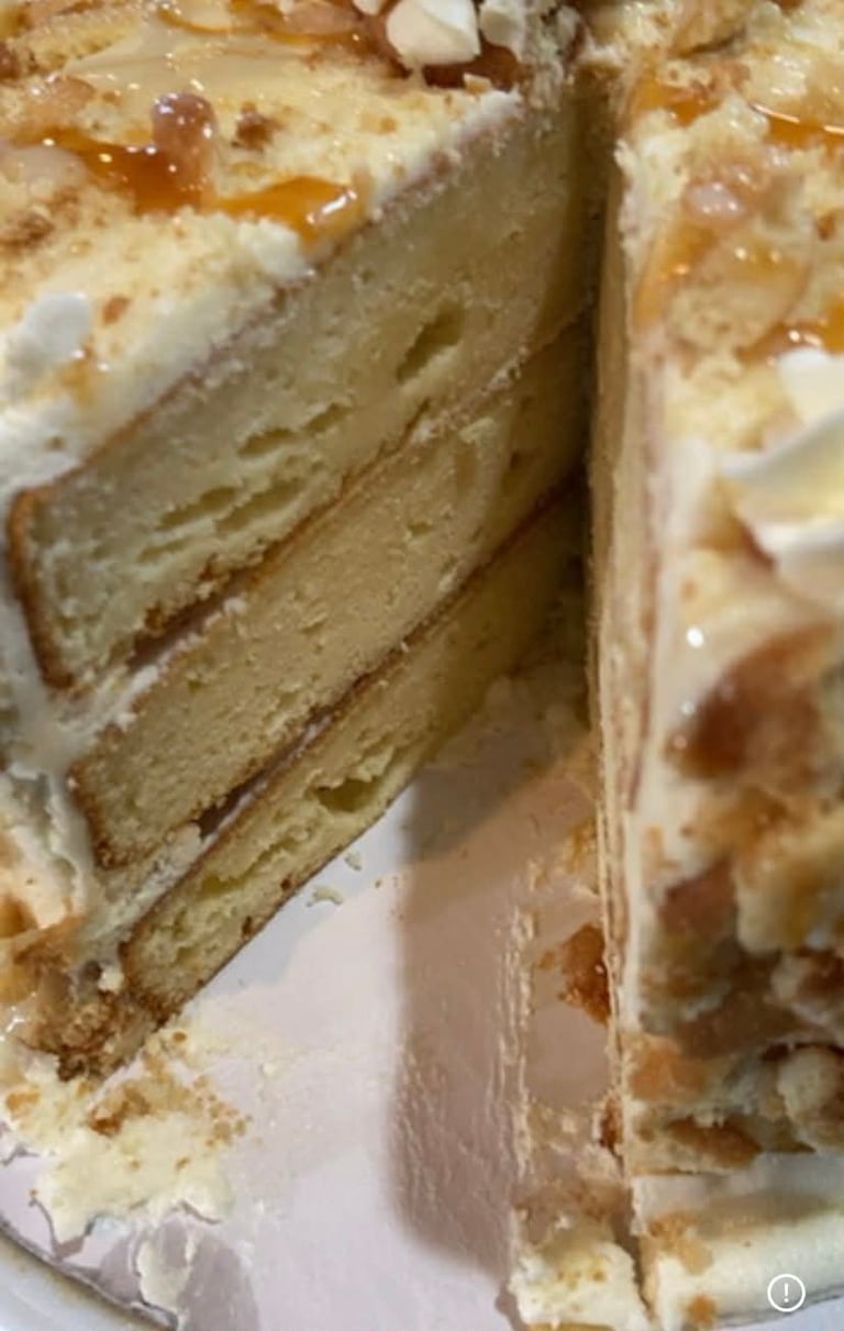 Close-up of a layered cake with caramel drizzle, sliced to show the soft, cream-colored cake layers and frosting