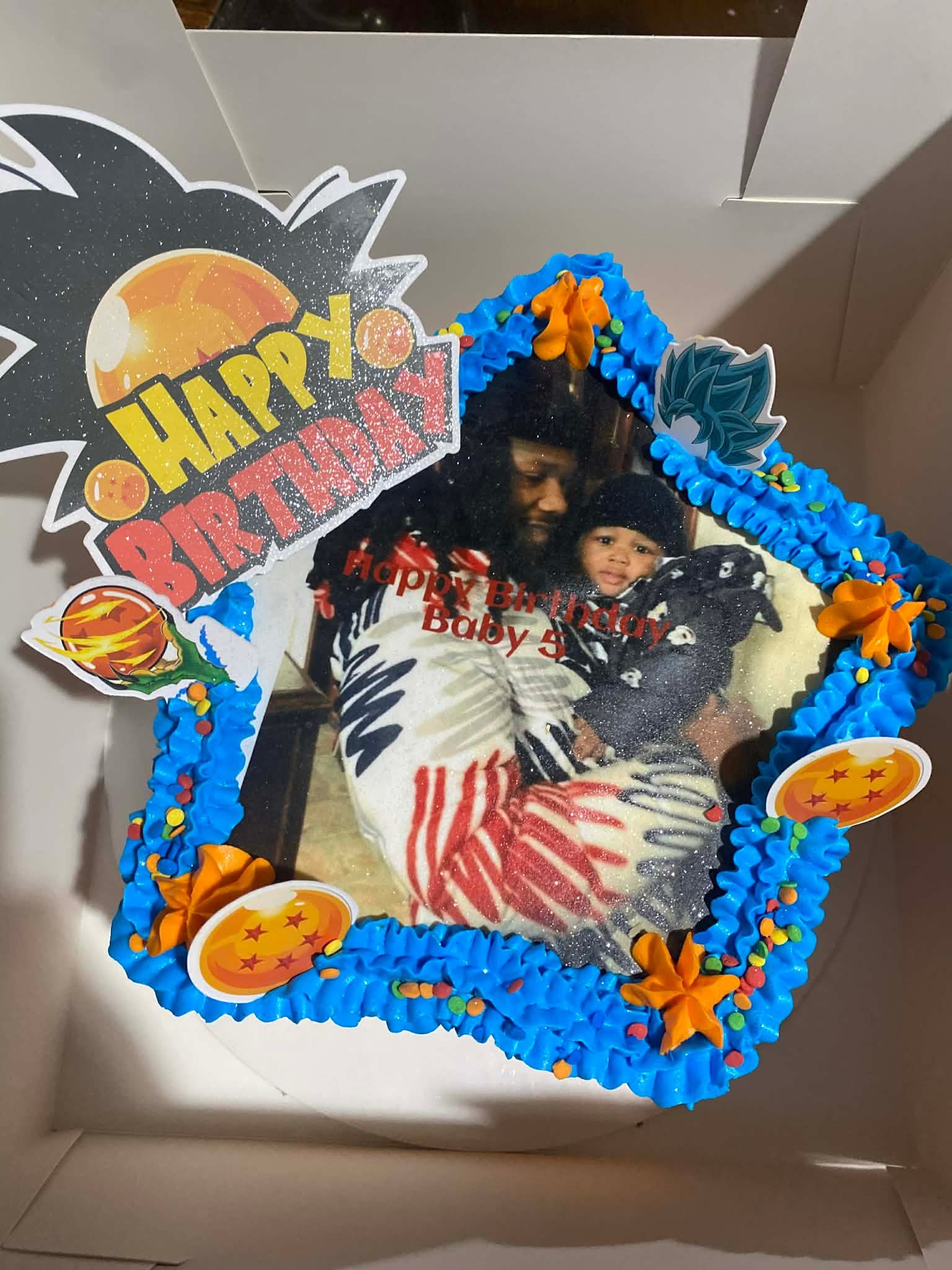Custom star-shaped birthday cake with blue frosting, edible image of characters, orange stars, and Happy Birthday decorations