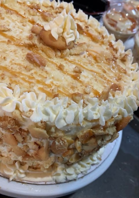 Multi-layered cake with caramel frosting, topped with chopped nuts and white piped frosting swirls on a white plate