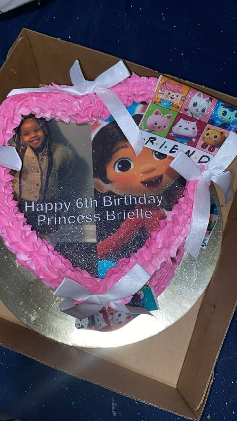 Heart-shaped birthday cake with pink ruffled frosting, white bow, and edible image saying Happy 6th Birthday Princess Brielle, decorated with character toppers