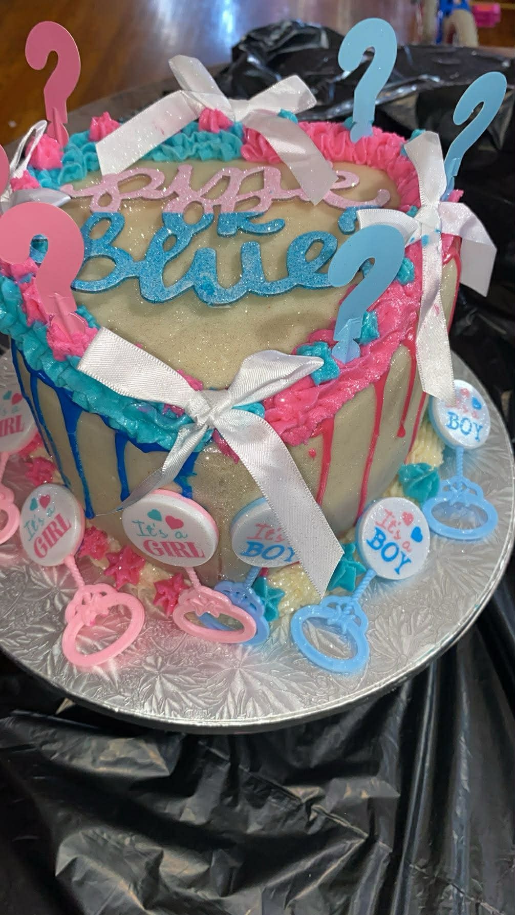 Gender reveal cake with blue and pink decorations, question marks, and Baby text on gold fondant