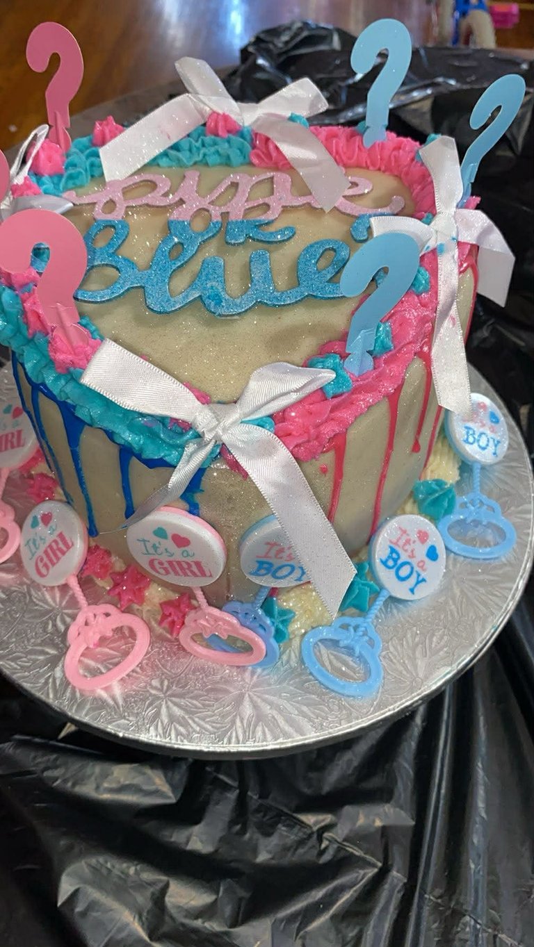 Gender reveal cake with blue and pink decorations, question marks, and Baby text on gold fondant